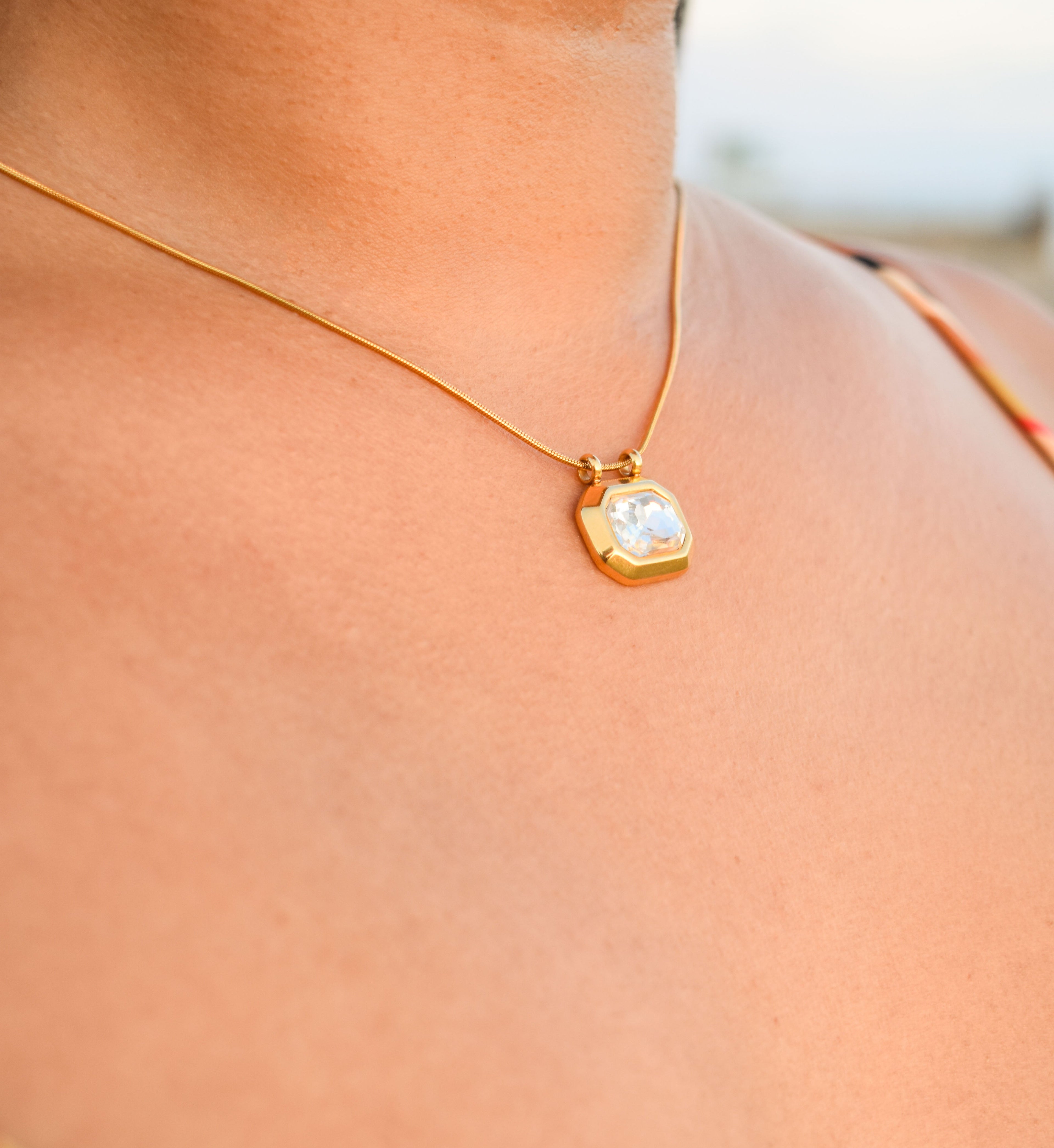 Gold necklace with a pendant on a person wearing a striped garment.