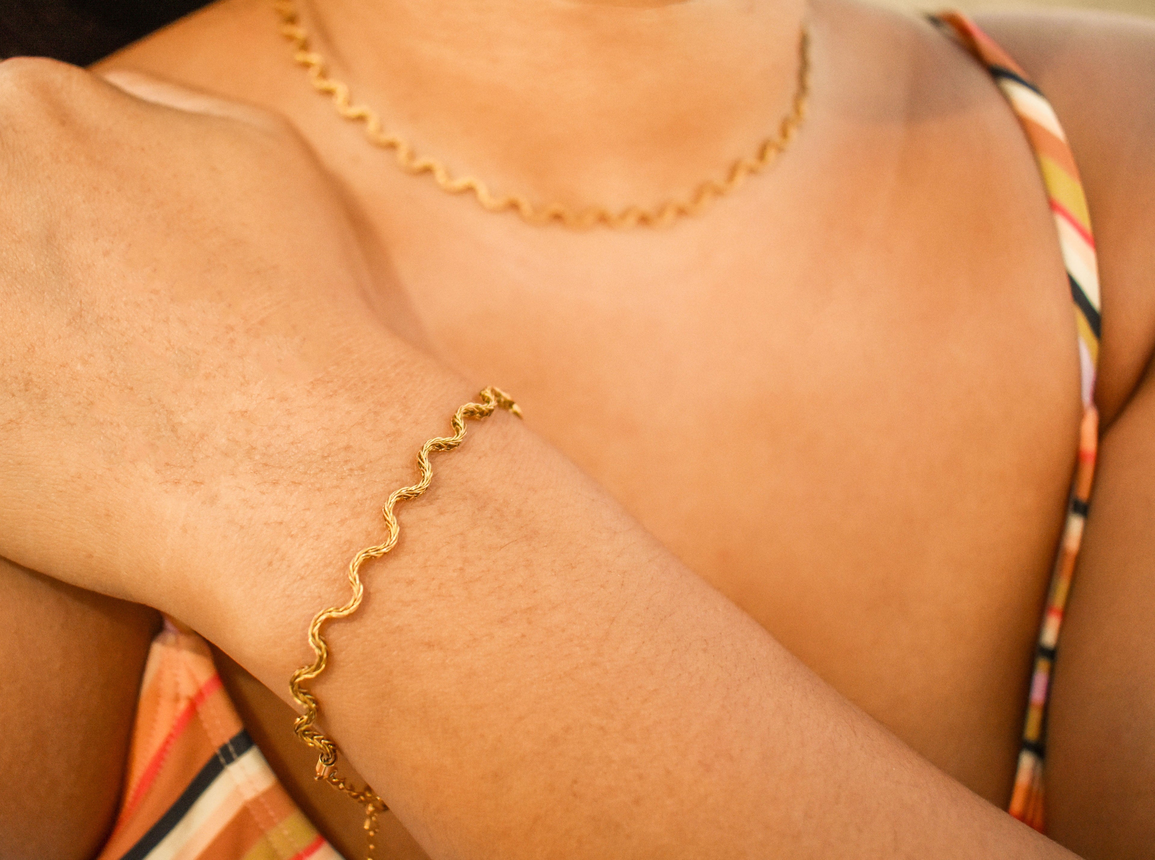Close-up of a person wearing a gold bracelet and necklace.
